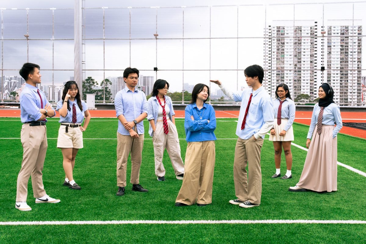 Friends spread across a rooftop football pitch, some posing, with tower blocks behind.