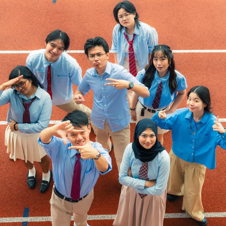 Friends seen from above on a red running track, striking playful poses and looking up at the camera.