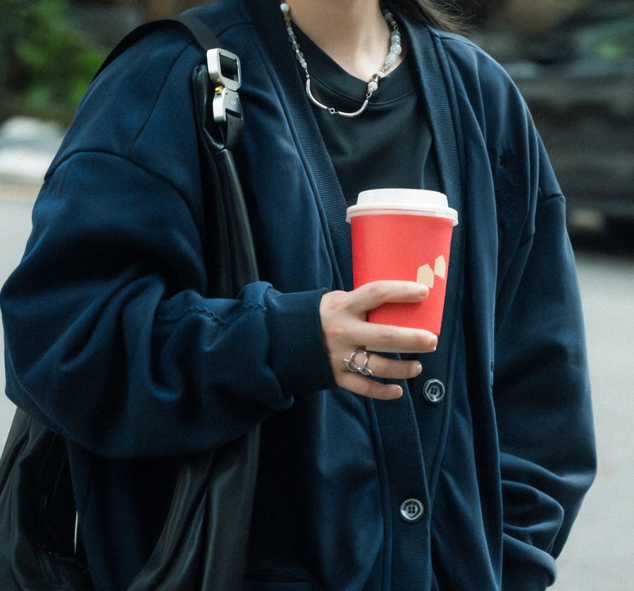Close crop of the navy cardigan, a silver clasp on the bag strap, a ring and the red cup.