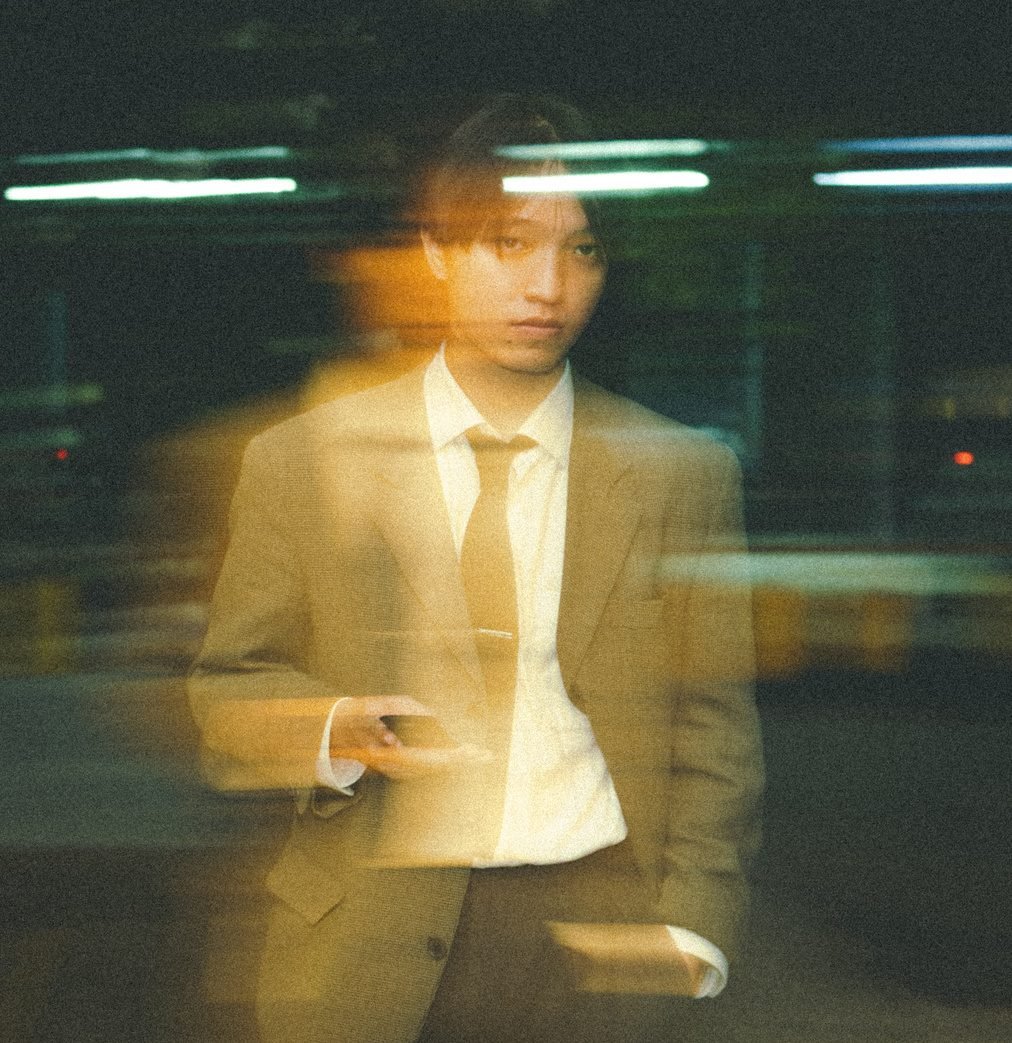The same man in the suit, smeared with amber motion blur, his face sharp, with white strip lights streaking behind him.