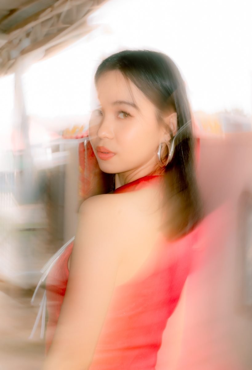 A woman in a red halter top glances back over her shoulder, the whole frame swept into a soft pink and white blur.